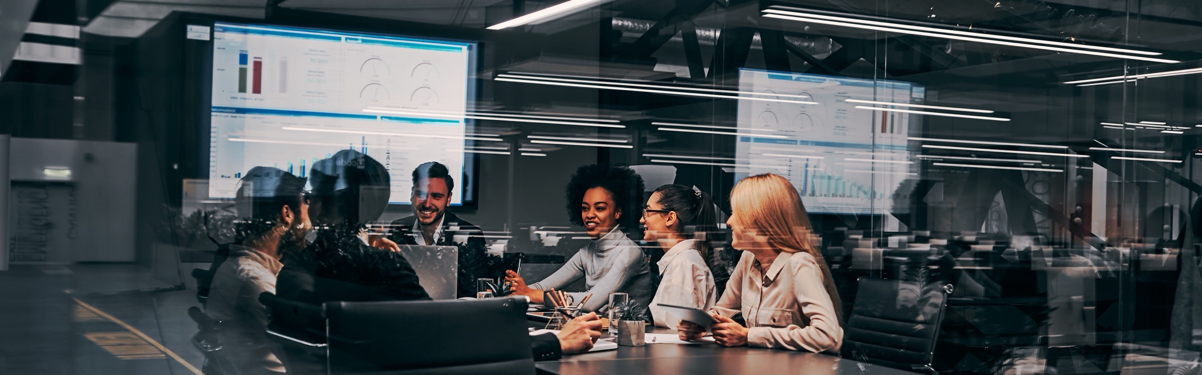 A finance team meeting around a table with reporting dashboards on screens behind them.