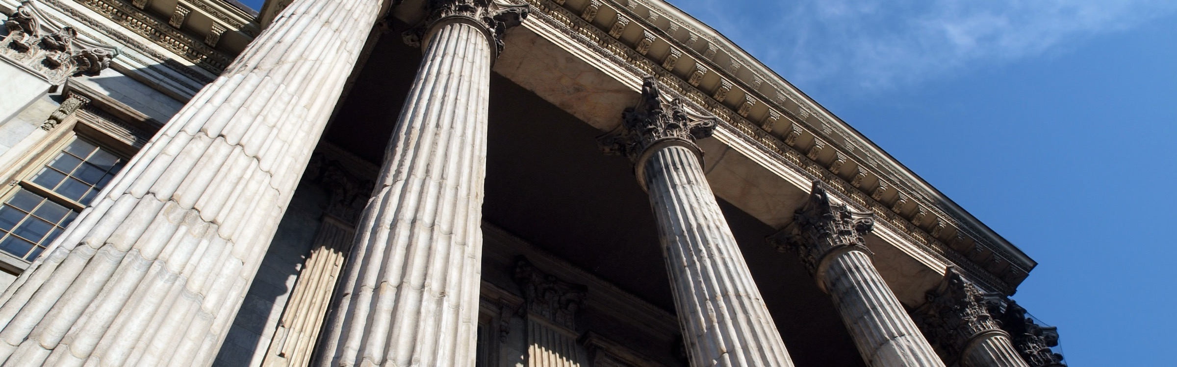 Looking up at the columns and cornice of a classical institutional building against a blue sky.