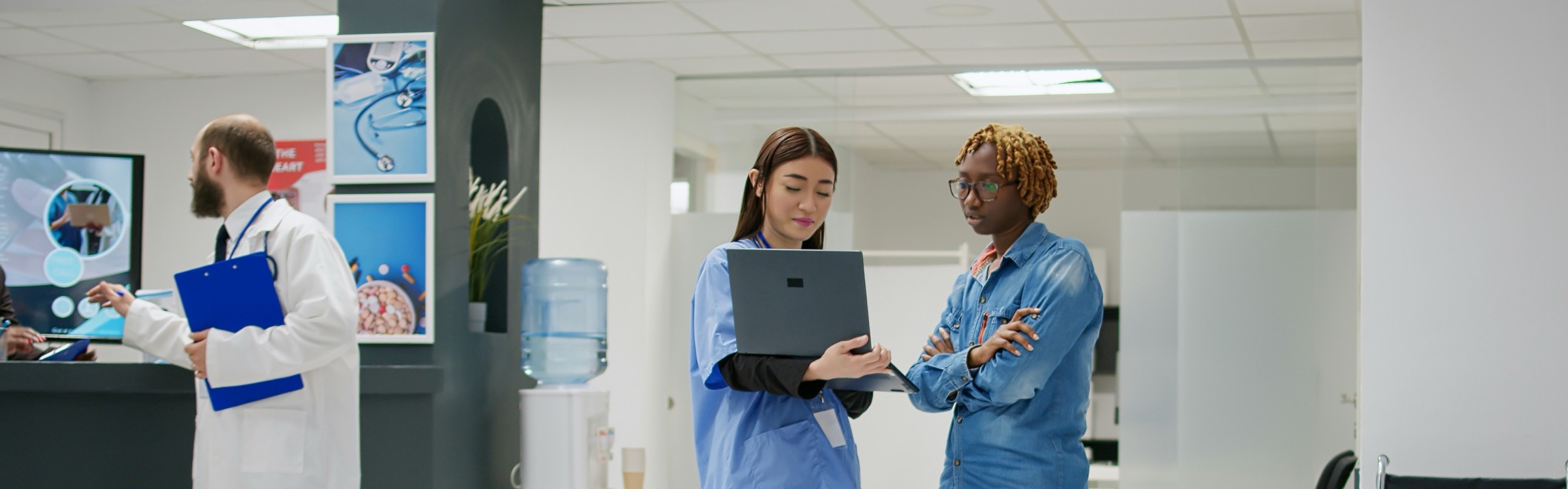 A clinician and a colleague reviewing a patient case together on a laptop in a hospital waiting area.
