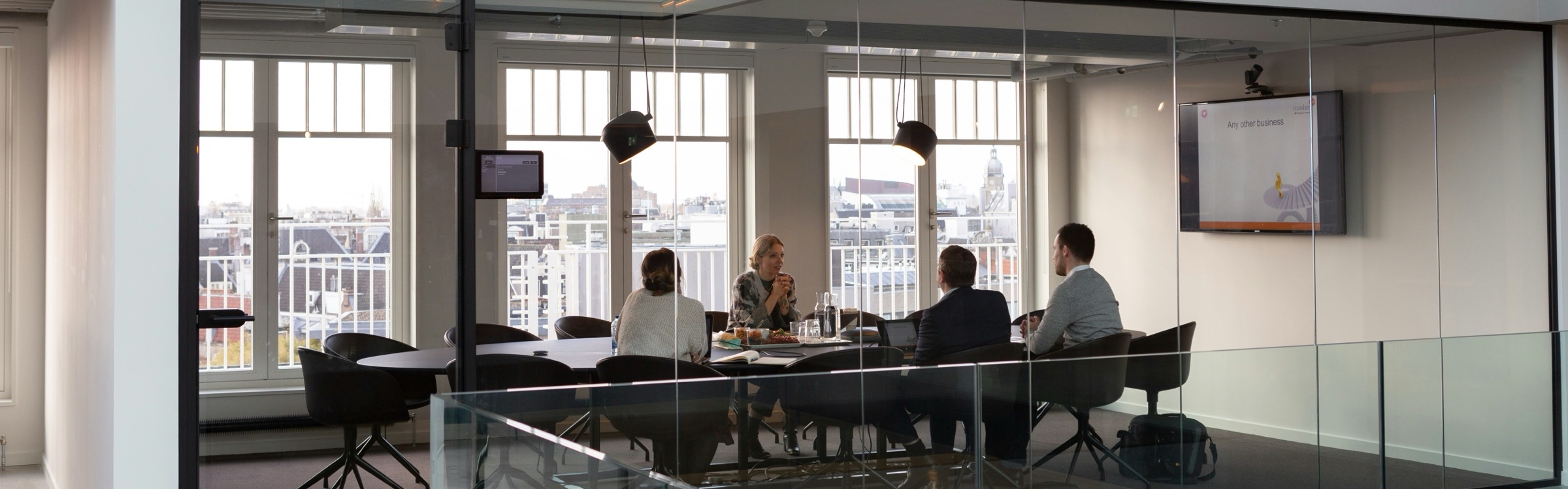 A team meeting around a table in a glass-walled conference room with a city view.