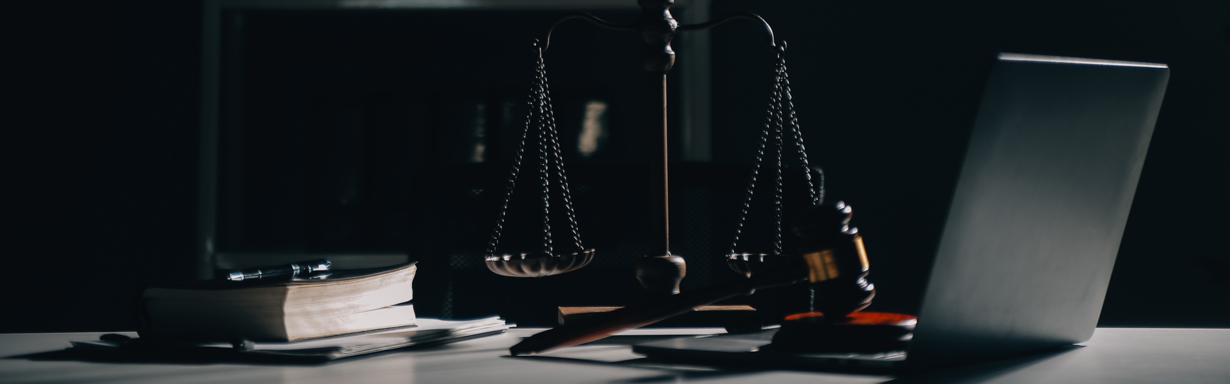 Scales of justice and a gavel on a desk beside a law book and an open laptop.