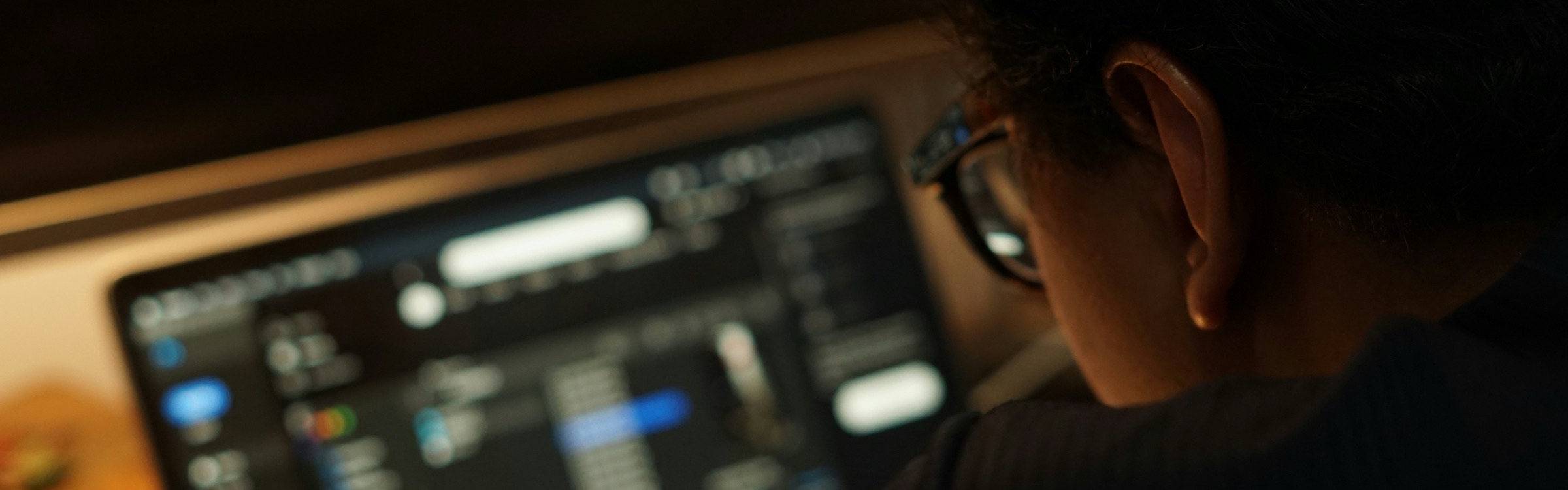 Someone working late on a laptop, editing timelines and levels in a dark room.
